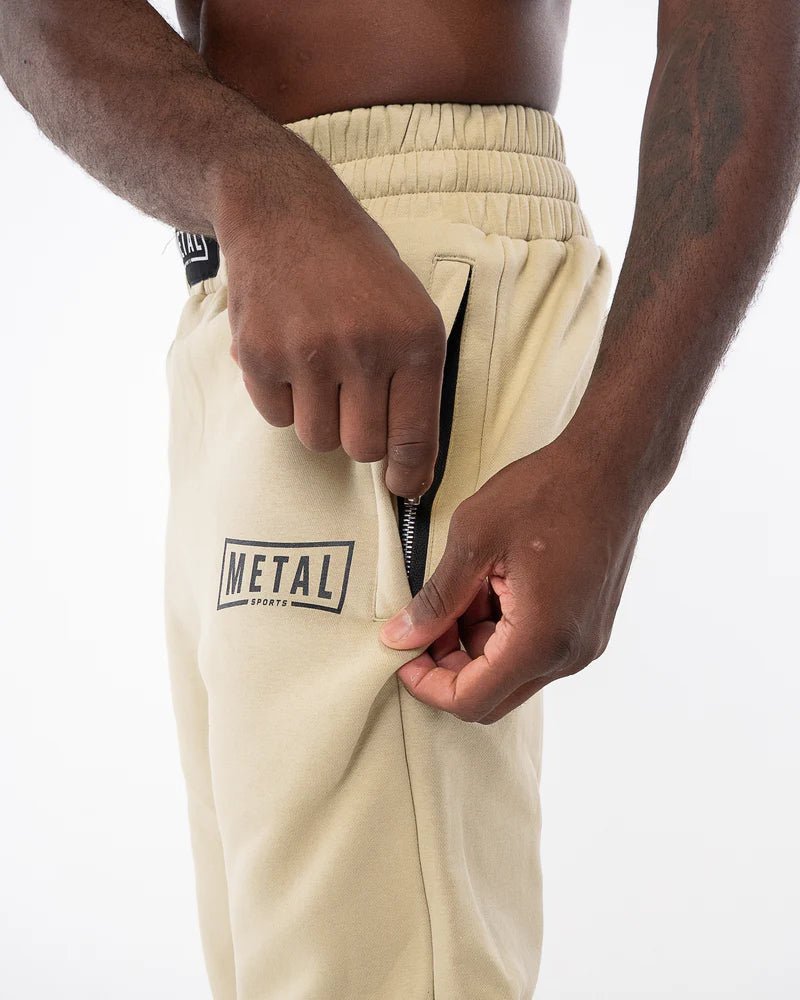 Detalle de cinturón fruncido y bolsillo invisible con cremallera en pantalones de chándal Metal Boxe beige