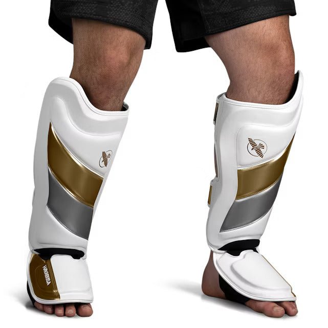 Vista frontale del parastinco Hayabusa T3 Striking bianco e oro, che mostra l'imbottitura pre-curvata