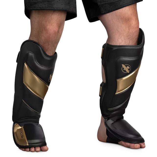 Vista frontale del parastinco Hayabusa T3 Striking nero e oro, che mostra l'imbottitura pre-curvata