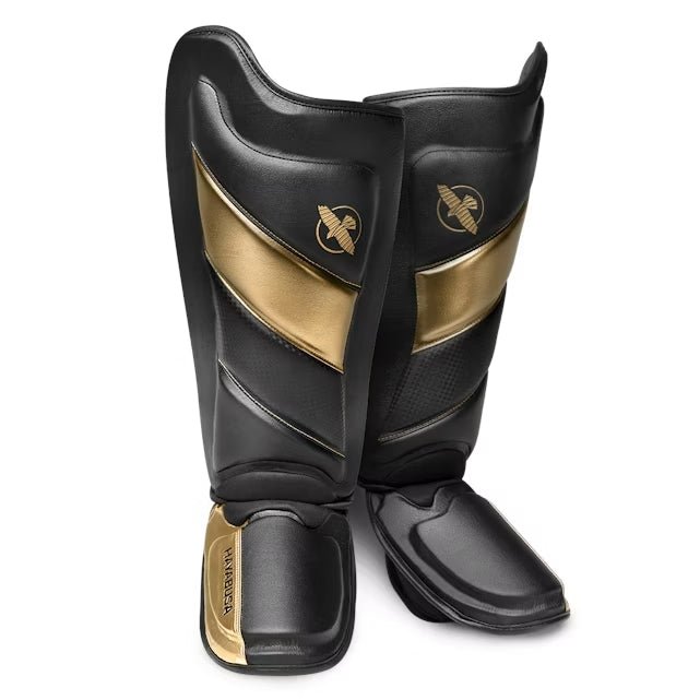 Par de espinilleras Hayabusa T3 Striking negras y doradas para kickboxing y MMA, vista frontal
