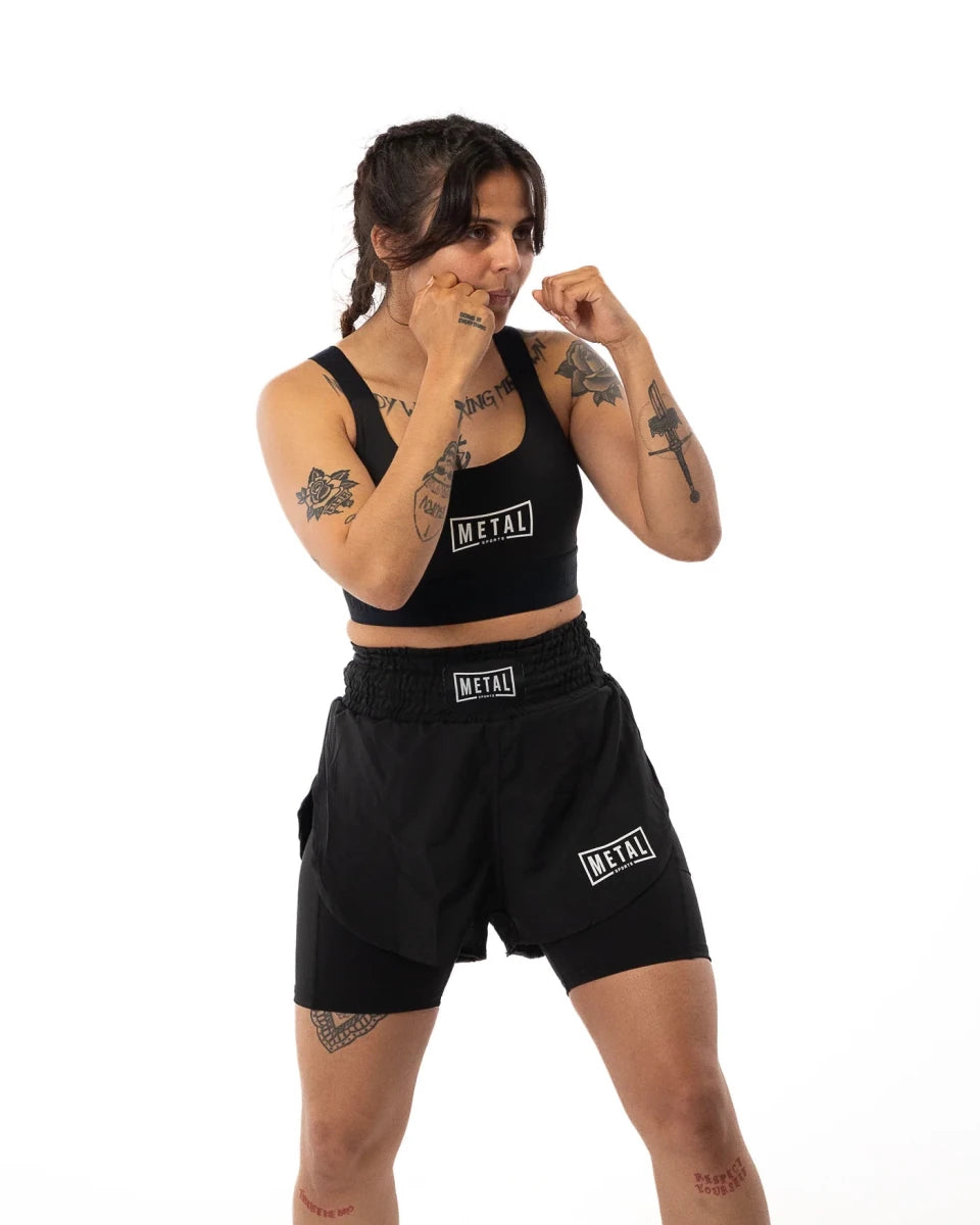 Atleta femenina en posición de guardia con pantalones cortos de boxeo de metal 2 en 1 negros